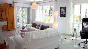 Ein modernes Wohnzimmer mit einem weißen Sofa, einem Glastisch, einer Holzkommode und einem Schreibtisch mit Stuhl.