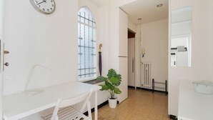 A room with a white desk, a potted plant, a clock, and a radiator.