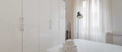Habitación de hotel con cama, armario, lámpara y ventana con cortinas.