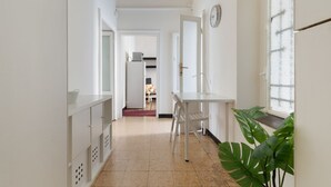 A hallway with a white desk, chairs, a clock, and a window with a plant.