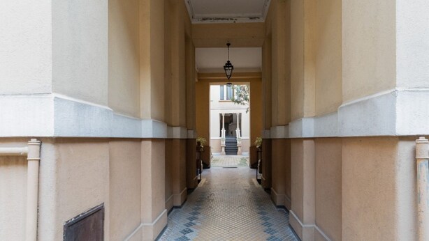 A corridor with patterned flooring, columns, and a staircase in the distance.