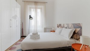 A hotel room with a bed, a bedside table, a lamp, a wardrobe, and a window with curtains.