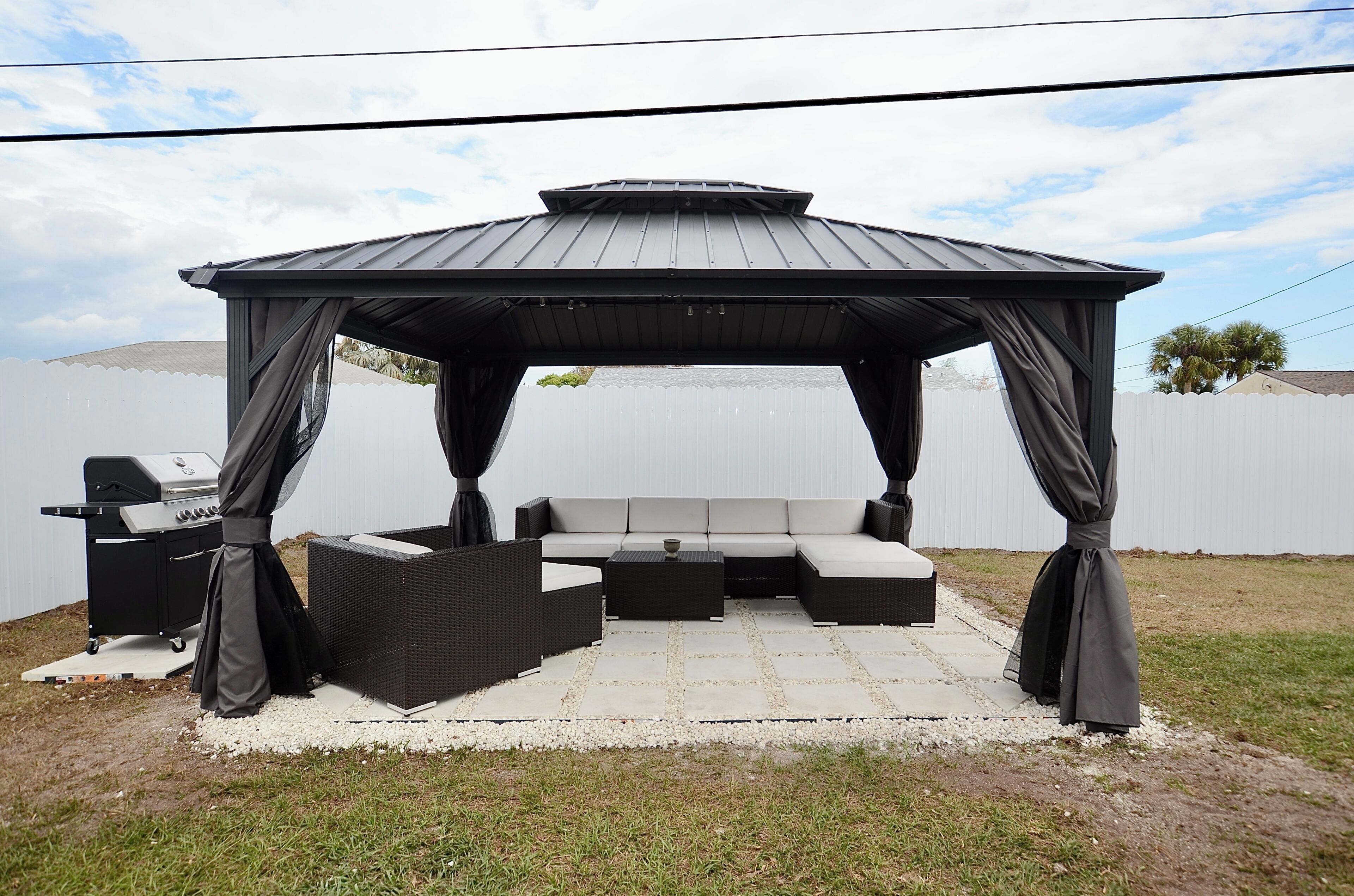A covered outdoor seating area with a grill, a sofa, and a coffee table.