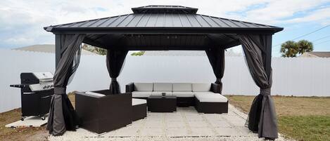A covered outdoor seating area with a grill, a sofa, and a coffee table.