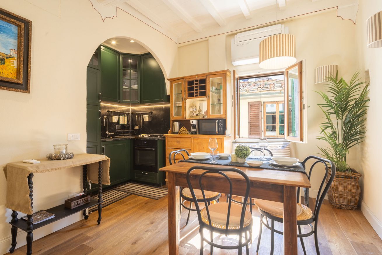 Una cocina acogedora con armarios verde oscuro, una mesa de comedor de madera y un amplio ventanal.