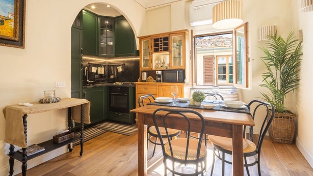 A cozy kitchen with dark green cabinets, a wooden dining table, and a large window. - Tornabuoni Cozy Apartment (Firenze)