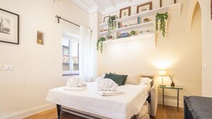 A neatly made bed with towels, a bedside table with a lamp, and a shelf with books and plants. - Tornabuoni Cozy Apartment (Firenze)