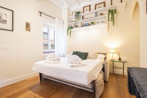A neatly made bed with towels, a bedside table with a lamp, and a shelf with books and plants. - Tornabuoni Cozy Apartment (Firenze)