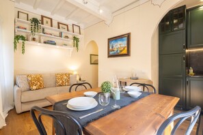 A dining area with a wooden table set for four, a sofa with patterned cushions, and shelves with books and plants. - Tornabuoni Cozy Apartment (Firenze)