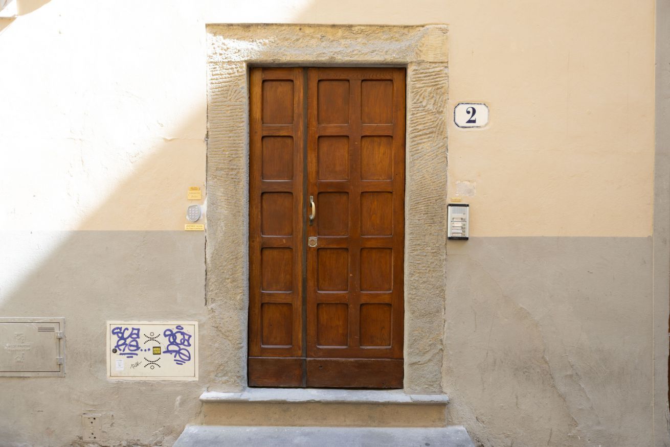 A double wooden door with a number '2' above it, set in a beige wall with a small window below.