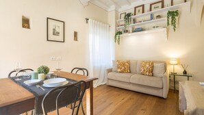 A dining area with a wooden table set for two, a sofa with patterned cushions, and a bookshelf with plants. - Tornabuoni Cozy Apartment (Firenze)