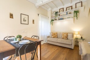 A dining area with a wooden table set for two, a sofa with patterned cushions, and a bookshelf with plants. - Tornabuoni Cozy Apartment (Firenze)