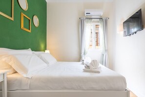 A neatly made bed with white linens, a wall-mounted TV, and a window with curtains. - Tornabuoni Cozy Apartment (Firenze)