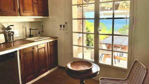 A kitchen with wooden cabinets, a sink, and a window overlooking a patio with a table and chairs. - Villa with sea and Esterel views: 5 bedrooms, swimming pool, air conditioning. (Saint-Raphaël)