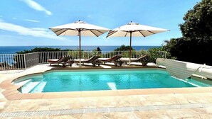 A swimming pool with lounge chairs and umbrellas, surrounded by a white fence, with a view of the ocean. - Villa with sea and Esterel views: 5 bedrooms, swimming pool, air conditioning. (Saint-Raphaël)