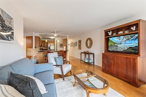 A living room with a sofa, chairs, a coffee table, a TV, and a kitchen in the background. - NEWLY UPDATED-GREAT LOCATION-WELL EQUIPPED-METICULOUS CLEANING-AC (Kihei)