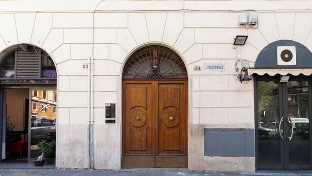 A building with a large wooden double door, a sign reading 'CONDOMINIO', and a small potted plant outside. - ReRent Rooms - 81 MANZONI GUESTHOUSE (Rome)