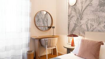 Une chambre à coucher comprenant un lit, un bureau, une chaise, un miroir rond, une lampe et une poubelle.