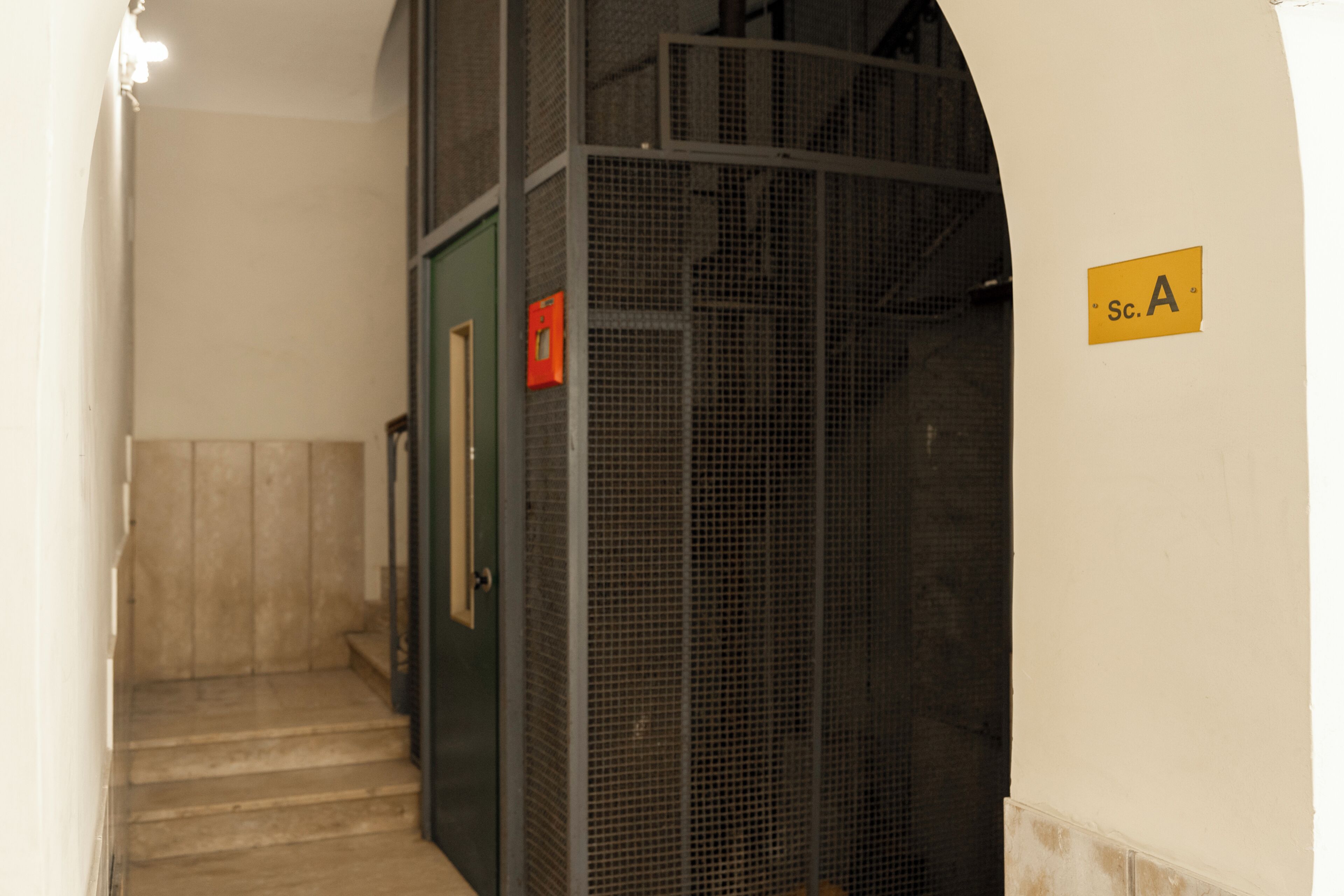 Eine Treppe führt zu einem Raum mit einer Metalttür und einem Schild, das die Zimmernummer A anzeigt.