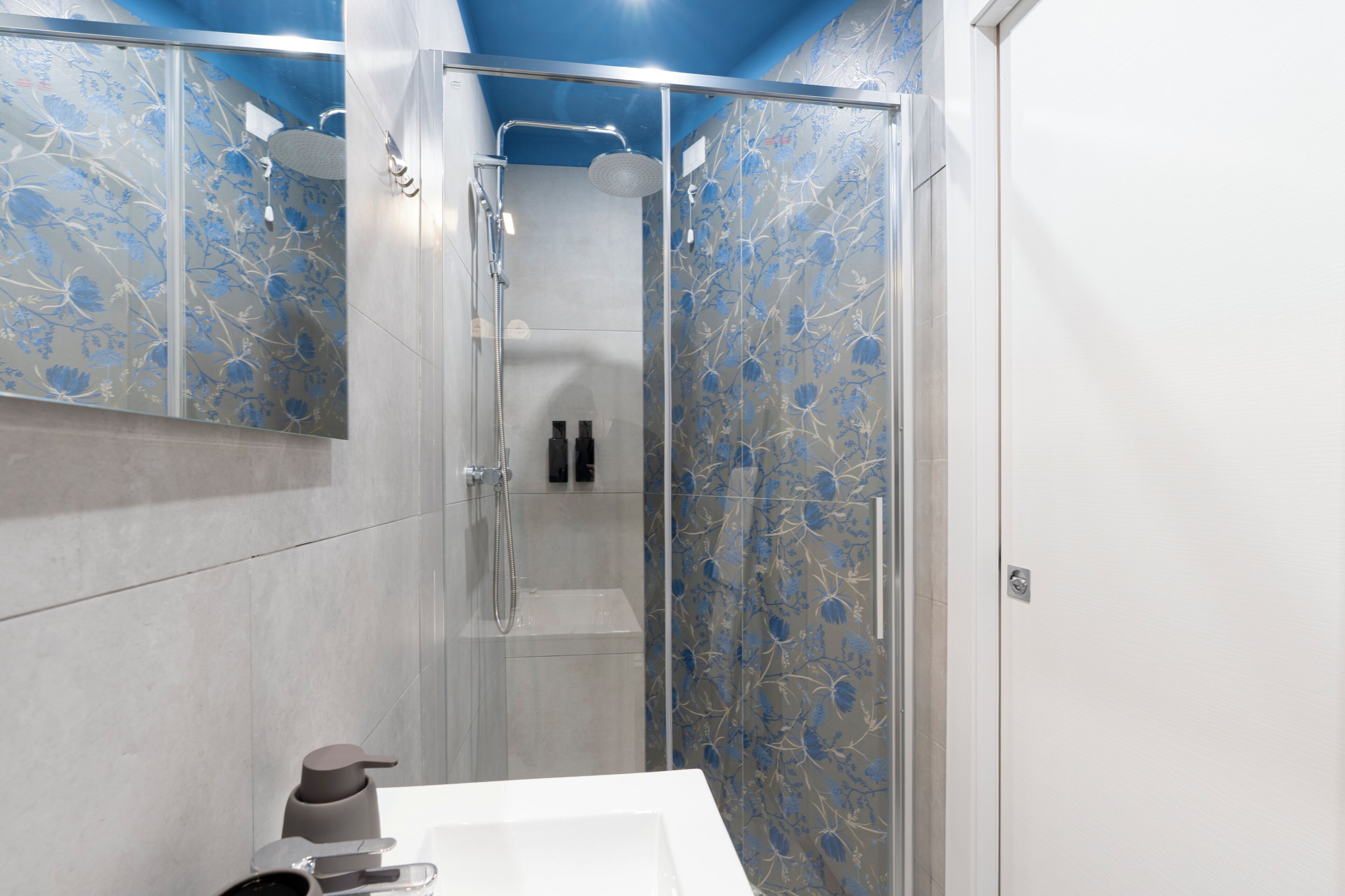 A modern bathroom with a glass shower enclosure, a white sink, and a mirror.