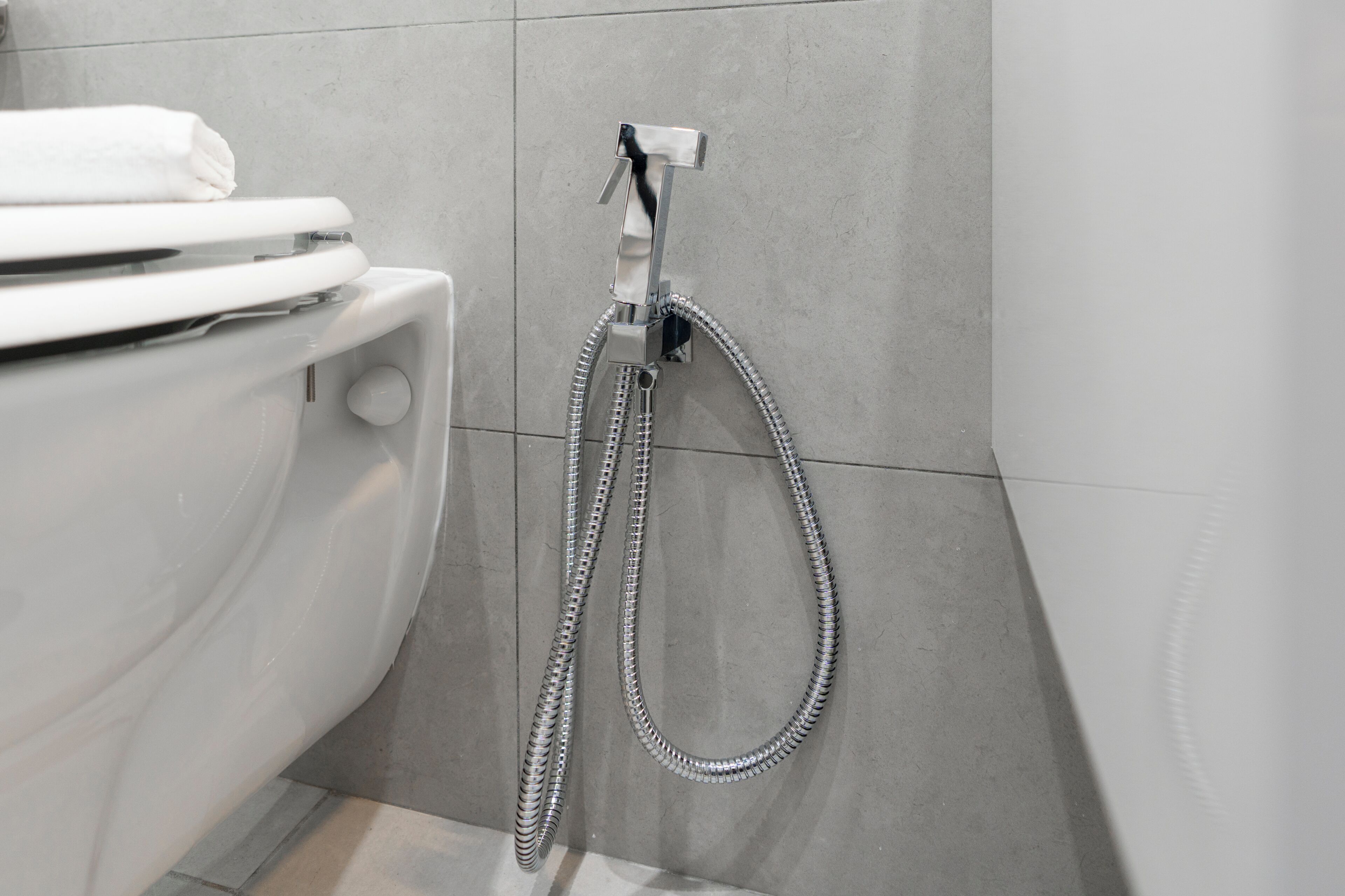 A modern bathroom with a toilet, a shower head, and a towel rack.