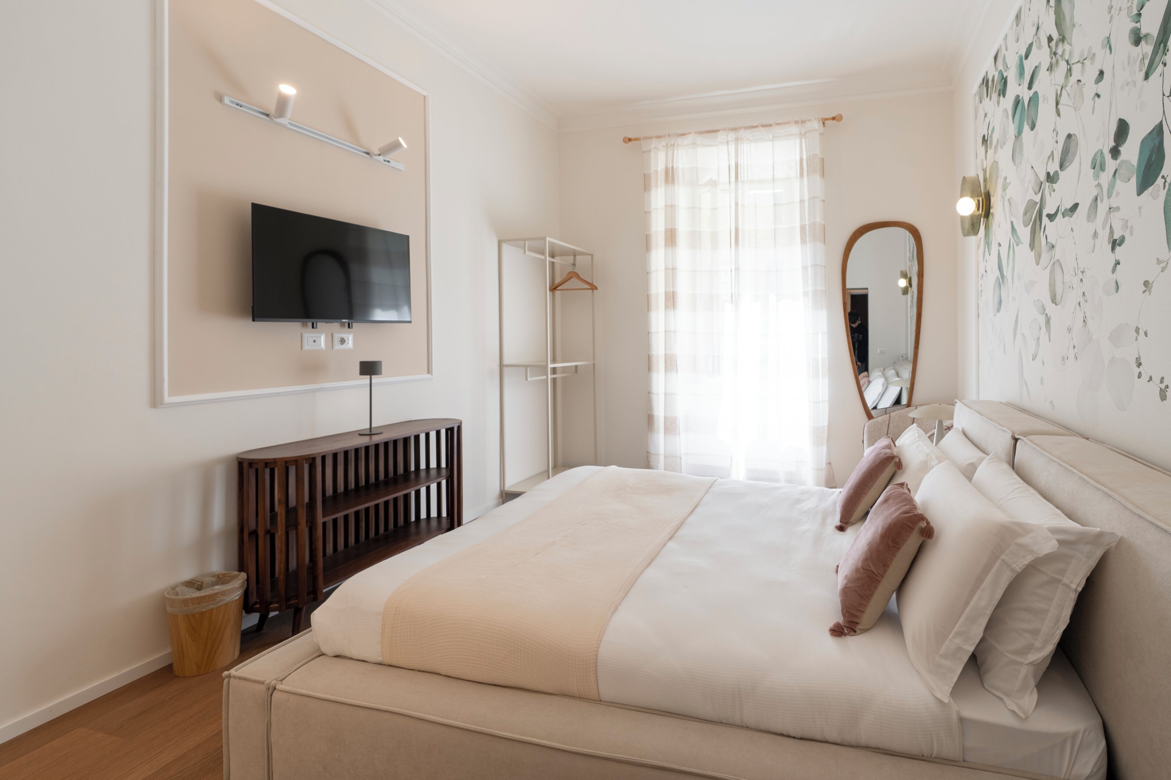 Ein Schlafzimmer mit Bett, Wandfernseher, Spiegel und einem Fenster mit Vorhängen.
