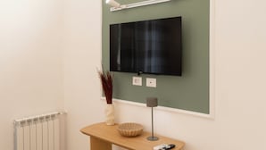 A room with a mounted flat-screen TV, a wooden console table with a vase and a bowl, and a floor lamp. - ReRent Rooms - 81 MANZONI GUESTHOUSE (Rome)