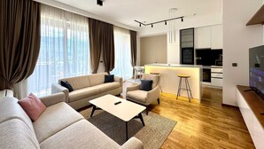 Un salon moderne comprenant un canapé, des fauteuils, une table basse et un coin cuisine avec un bar et un comptoir.