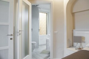 A hotel room with a bathroom visible through an open door, a bed, a bedside table, and a nightstand. - Tornabuoni Classic Apartment  (Firenze)