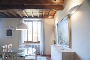 A dining area with a glass table, chairs, a pendant light, a radiator, and a window with curtains. - Tornabuoni Classic Apartment  (Firenze)
