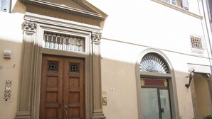 A building facade with a large wooden double door, a small window with a metal grille, and a small balcony with potted plants. - Tornabuoni Classic Apartment  (Firenze)