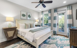 A bedroom with a bed, nightstands, a ceiling fan, and a view of the outdoors through a window with curtains. - Upscale Watercolor Home + Golf Cart, Bikes & Pools (Santa Rosa Beach)