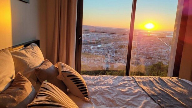 A bedroom with a large window overlooking a cityscape at sunset. - Le Rouquier Studio with exceptional view terrace (Sète)