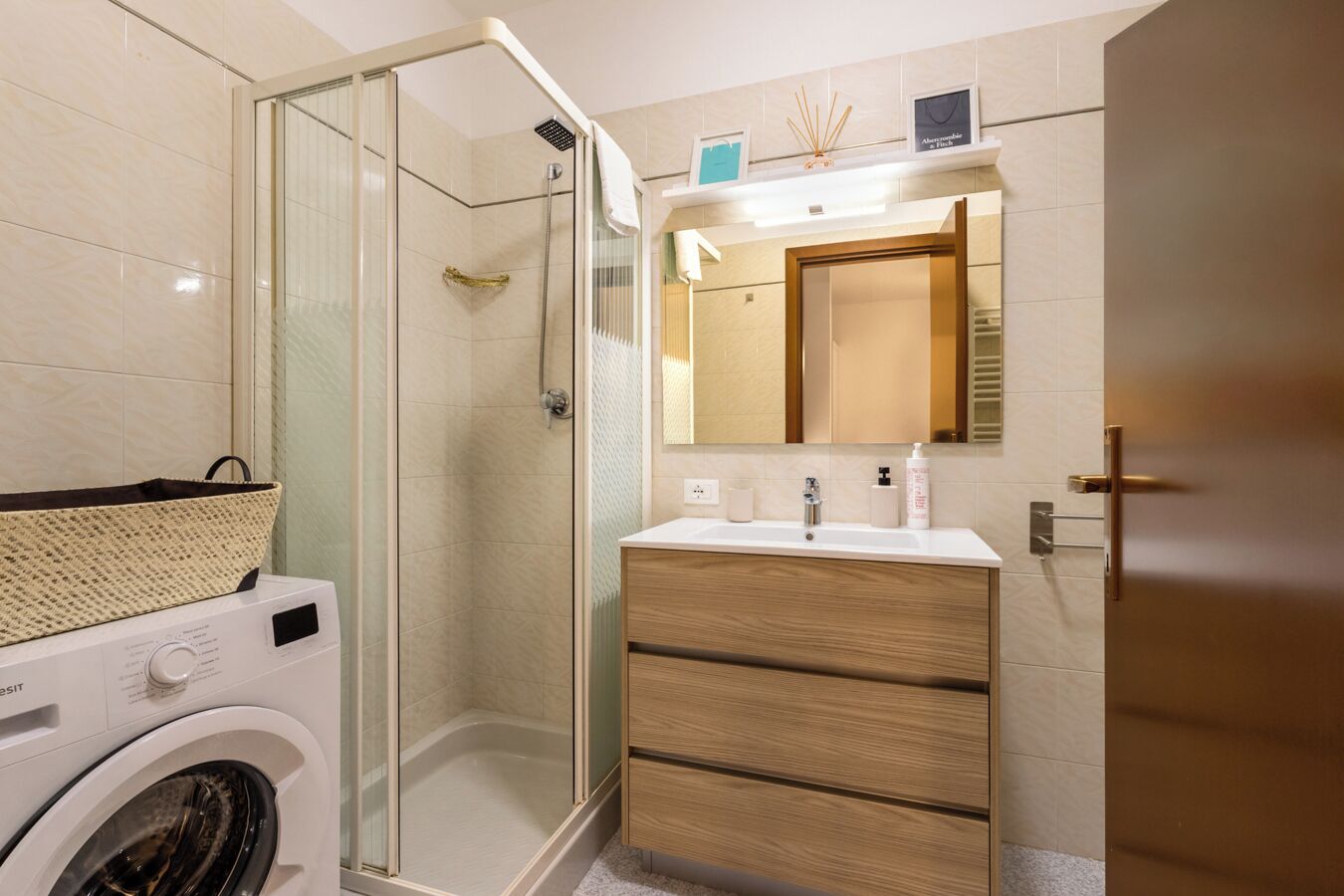 A modern bathroom with a glass-enclosed shower, a washing machine, and a wooden vanity with a mirror.