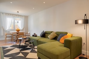 A modern living room with a green sofa, a dining table with chairs, a black floor lamp, and a patterned rug.