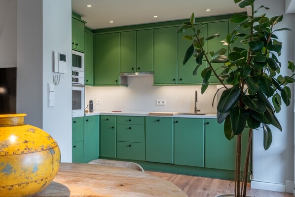 A kitchen with green cabinets, a yellow vase, and a potted plant.