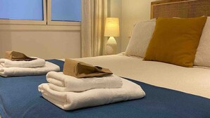 A hotel room with a bed, a nightstand with a lamp, a window with curtains, and towels on the bed. - Socaire Apartment in Ribadesella – Central, Renovated, Near the Beach (Ribadesella)