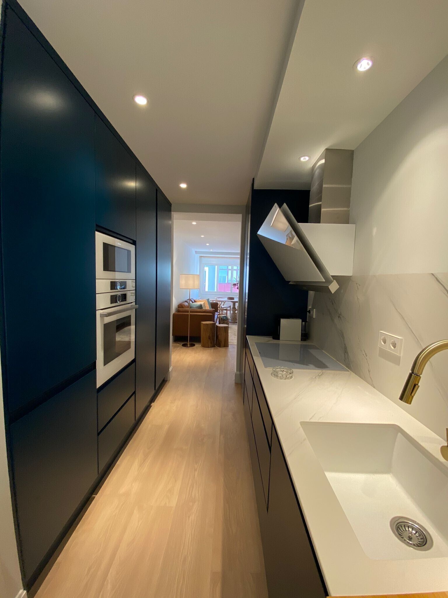Una cocina moderna con electrodomésticos integrados, un lavamanos blanco y una pared de color oscuro.