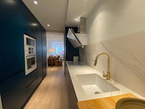 Eine moderne Küche mit weißer Arbeitsplatte, einem goldenen Wasserhahn und einem hölzernen Hocker.