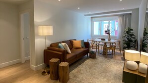 A modern living room with a brown sofa, a round coffee table, and a dining area with a white table and chairs. - Socaire Apartment in Ribadesella – Central, Renovated, Near the Beach (Ribadesella)