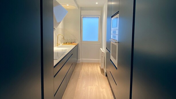 A narrow, modern kitchen with a window, a built-in oven, and a countertop with a sink. - Socaire Apartment in Ribadesella – Central, Renovated, Near the Beach (Ribadesella)