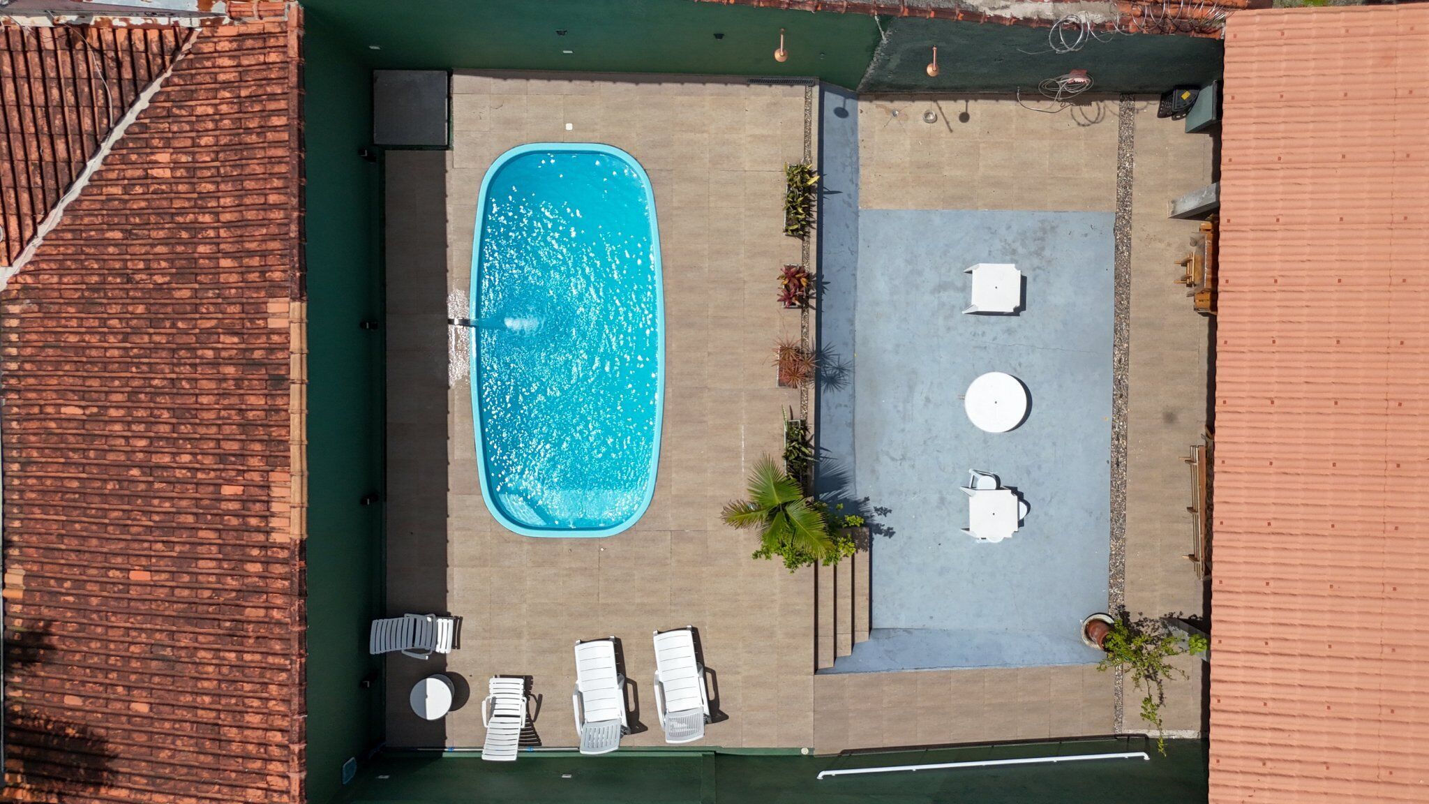 Vista aérea de un área de piscina con patio, sillas de descanso y una pequeña zona de estar.
