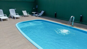 A swimming pool with a blue edge, surrounded by white lounge chairs and a small table.