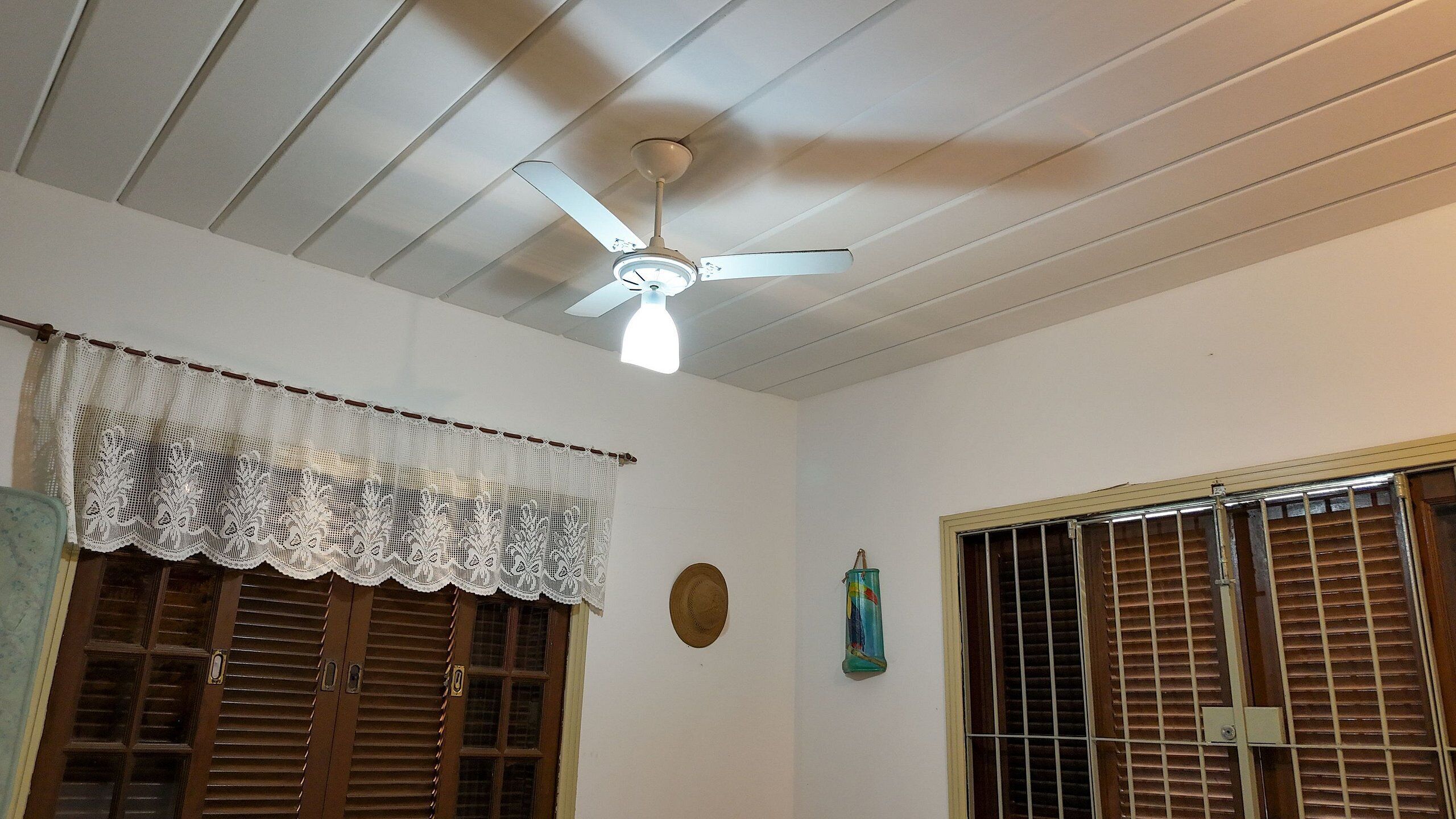 A room with a ceiling fan, wooden shutters, and a lace curtain.