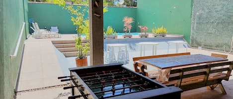An outdoor patio with a foosball table, seating area, and a pool.