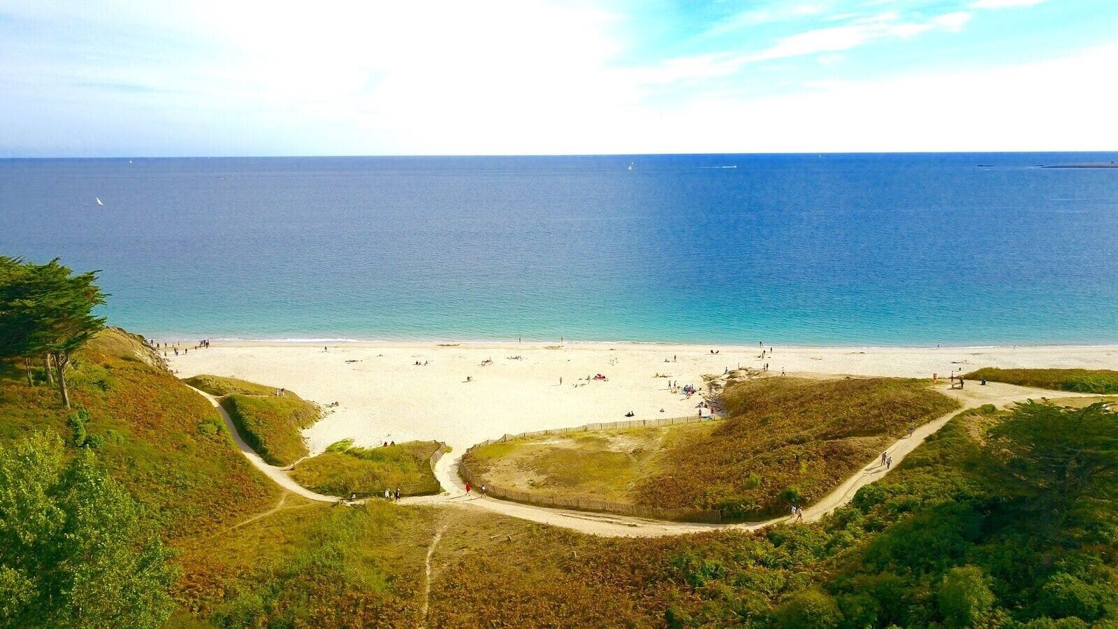 Une plage offrant une vue dégagée sur l’océan, une rive sablonneuse et un sentier menant à la plage.