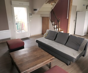 Un salon avec un canapé, une table en bois, un escalier et un coin cuisine.