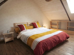 Une chambre avec un plafond en pente, un lit en bois recouvert d’une couette blanche et rouge, deux tables de chevet avec des lampes et un plancher en bois.