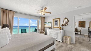 A bedroom with a large bed, a ceiling fan, a view of the ocean, a dresser, and a dining area. - 8th-Floor Beachfront Condo with Curved Balcony (Panama City Beach)