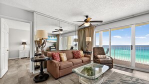A spacious living room with a large window, a ceiling fan, and a view of the ocean. - 8th-Floor Beachfront Condo with Curved Balcony (Panama City Beach)